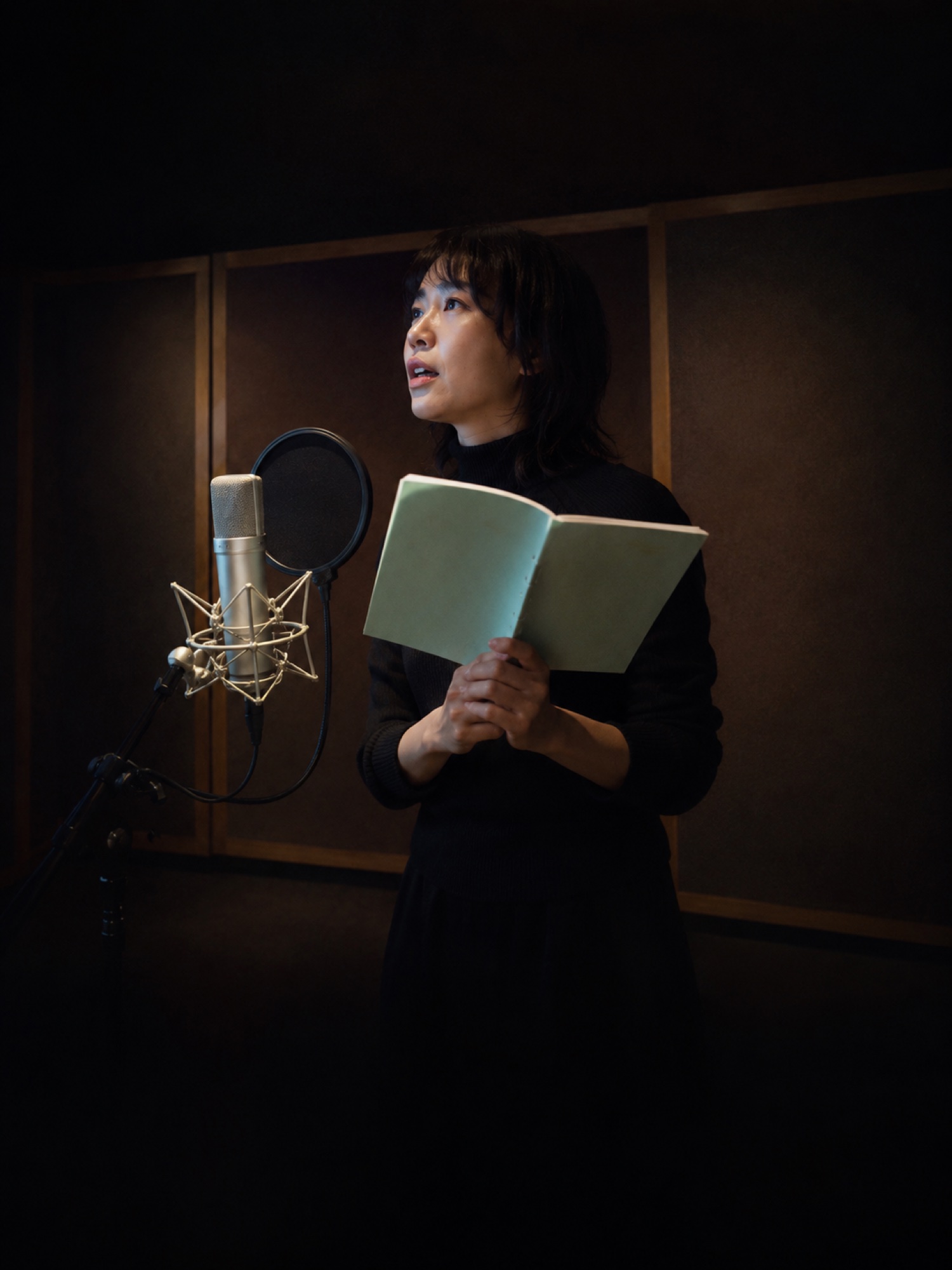 収録ブースで台本を手に立つ声優